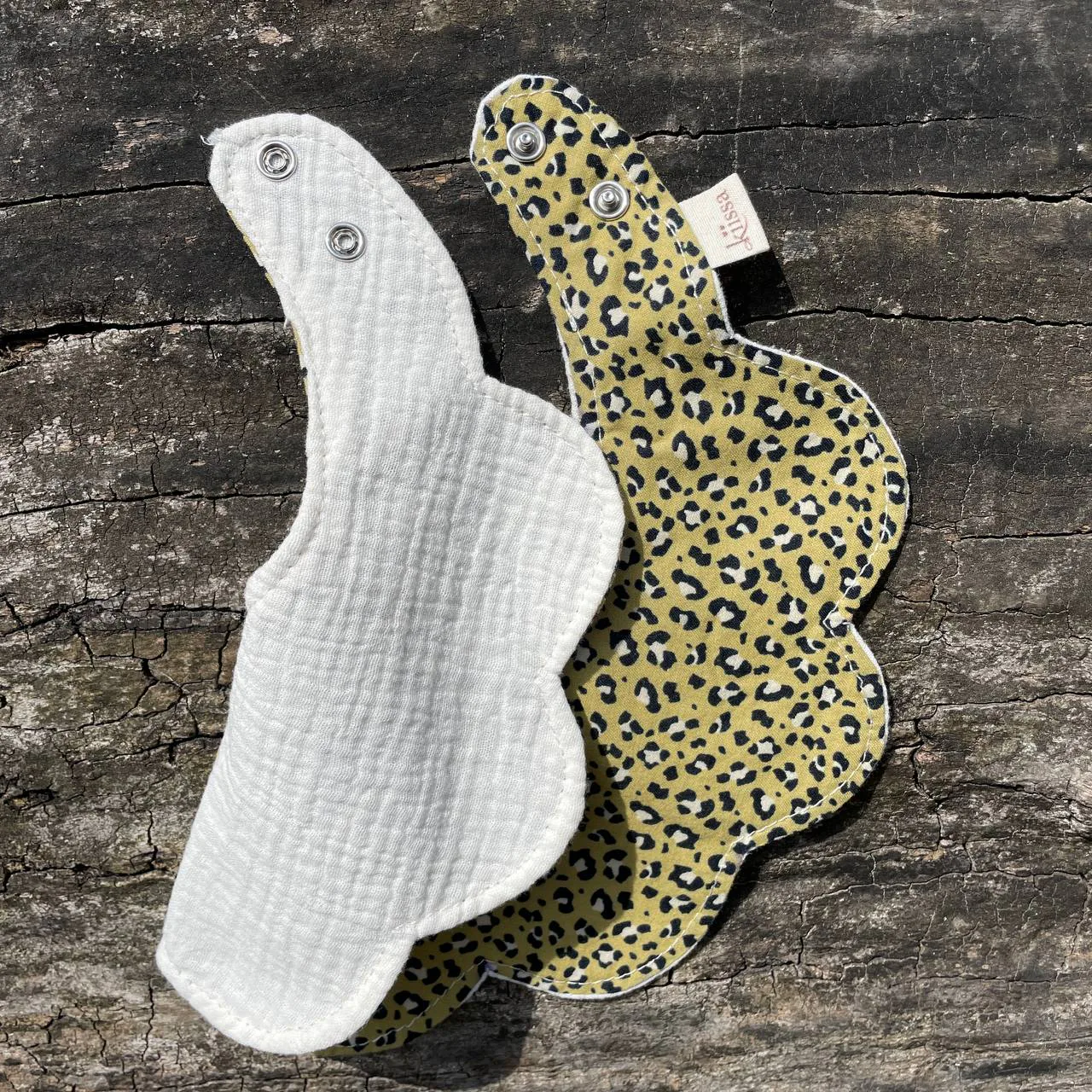 Two bibs on the log, one turned over to its white muslin back