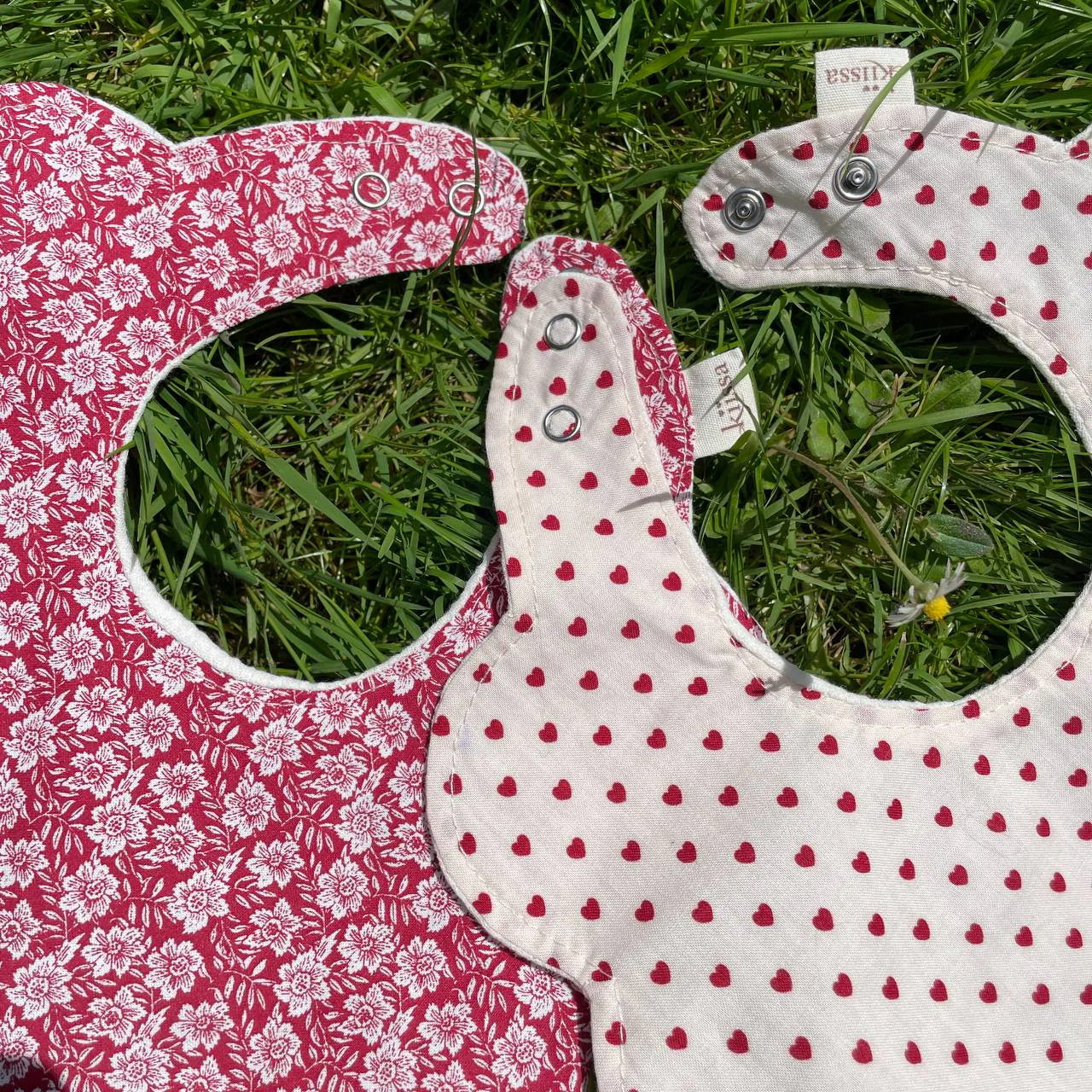 Close view of a red floral bib and a hearts bib in the grass