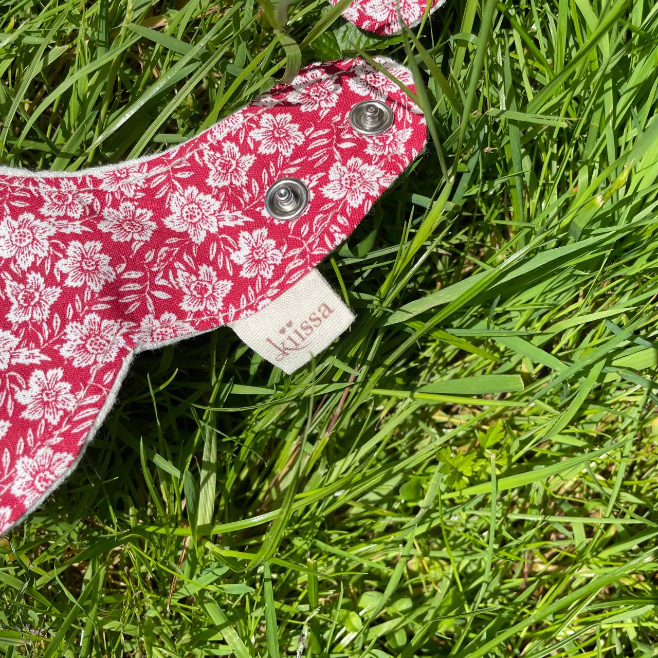 The snap and sewn-in Kiissa label of a red floral bib in the grass