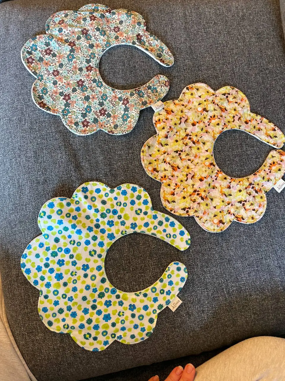Three flower bibs overlapping on a grey sofa