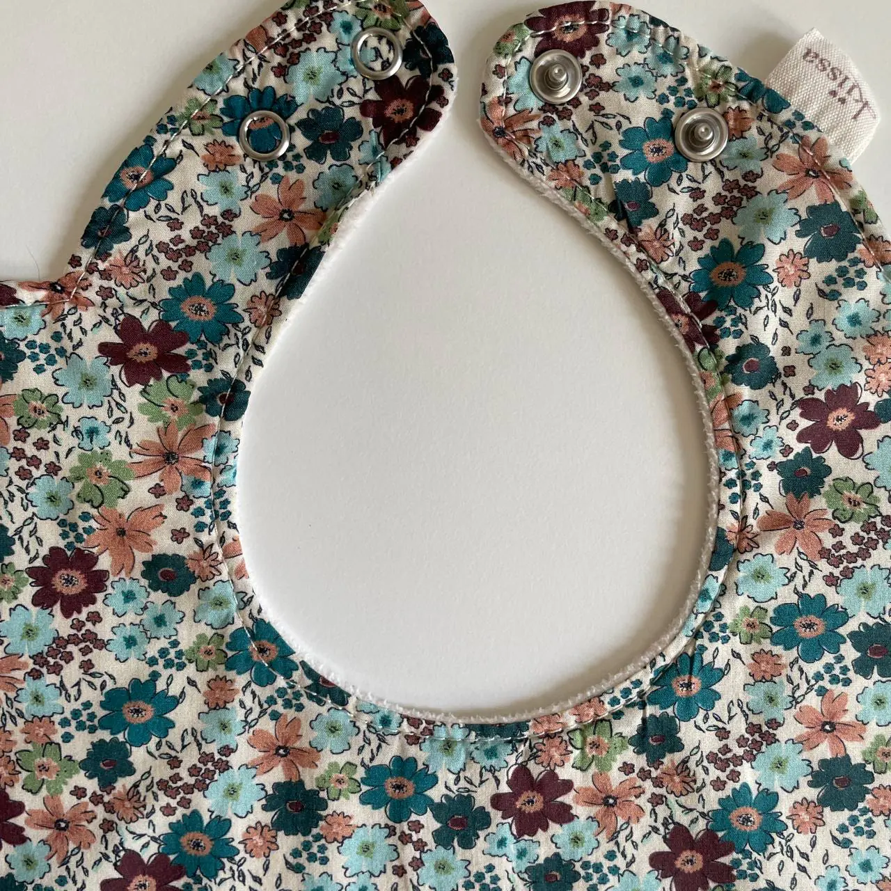 Close-up of stitching around the neckline of a teal floral bib
