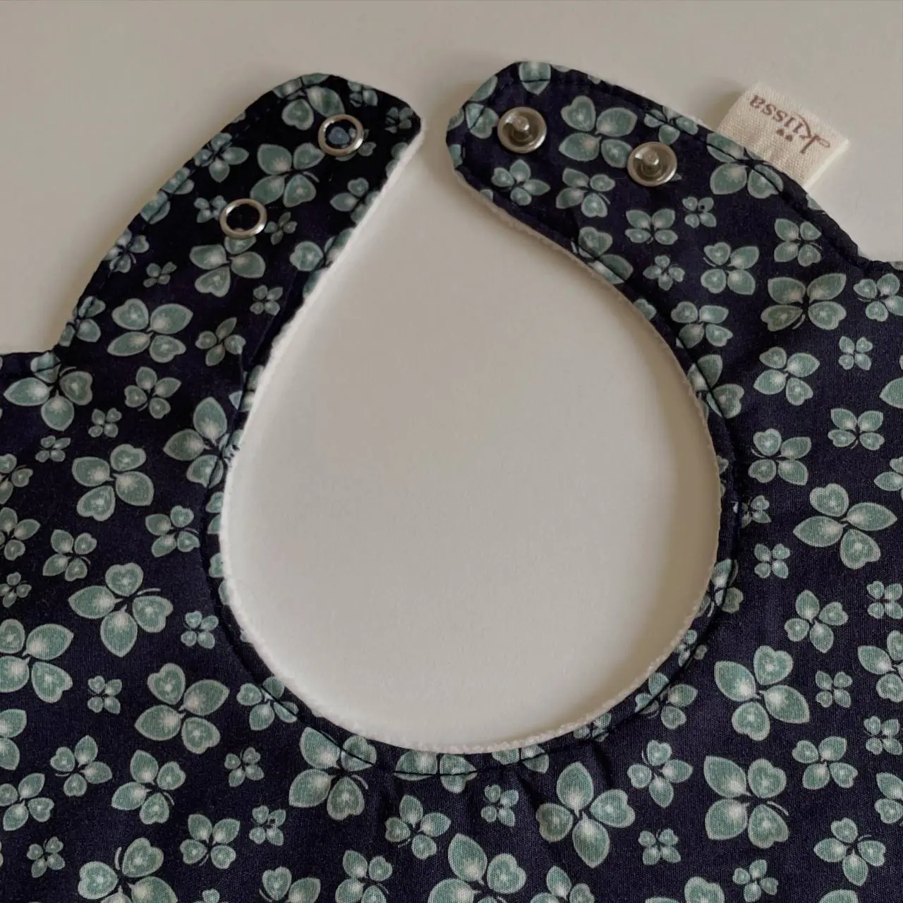 Close-up of the hand-set snap fastening on a navy floral bib